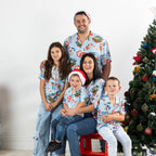 Family wearing matching faded blue Christmas Wishes Cheeky Santa festive shirts in a Christmas setting.