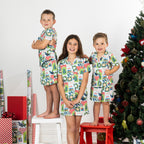 Three children wearing matching Christmas Wishes Tui Kids PJ Sets in white in a festive Christmas setting.