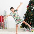 Boy wearing the Christmas Wishes Tui Kids PJ Set in white while posing beside a decorated Christmas tree.