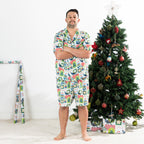 Man wearing the Christmas Wishes Tui Men’s PJ Set in white with arms crossed beside a decorated Christmas tree.