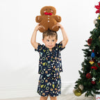 Boy wearing the Christmas Wishes Wreath Kids PJ Set in navy while holding a gingerbread cushion above his head.