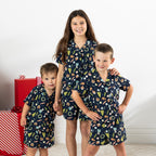 Three children wearing matching Christmas Wishes Wreath Kids PJ Sets in navy.