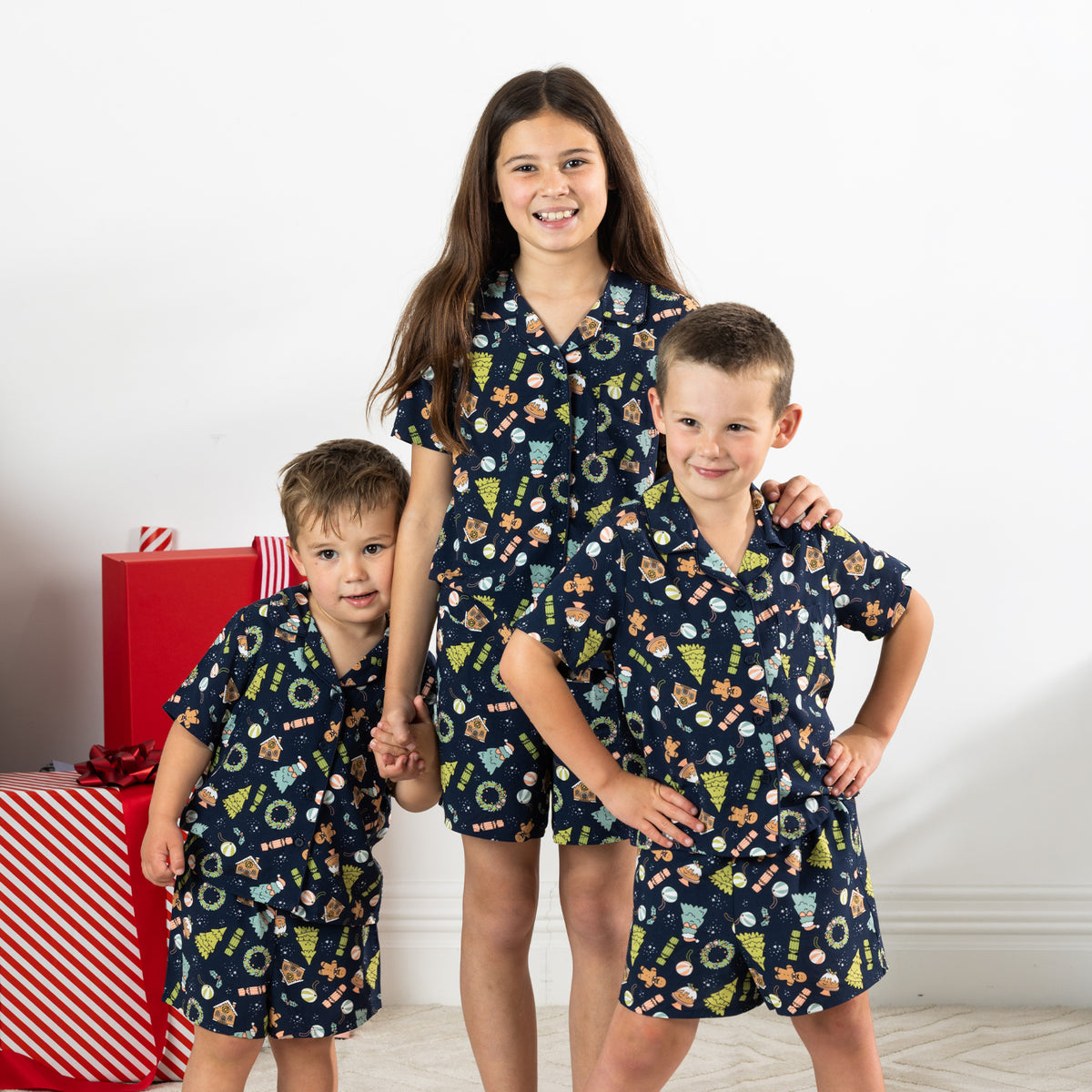 Three children wearing matching Christmas Wishes Wreath Kids PJ Sets in navy.
