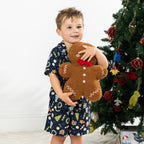 Boy wearing the Christmas Wishes Wreath Kids PJ Set in navy while holding a gingerbread cushion.