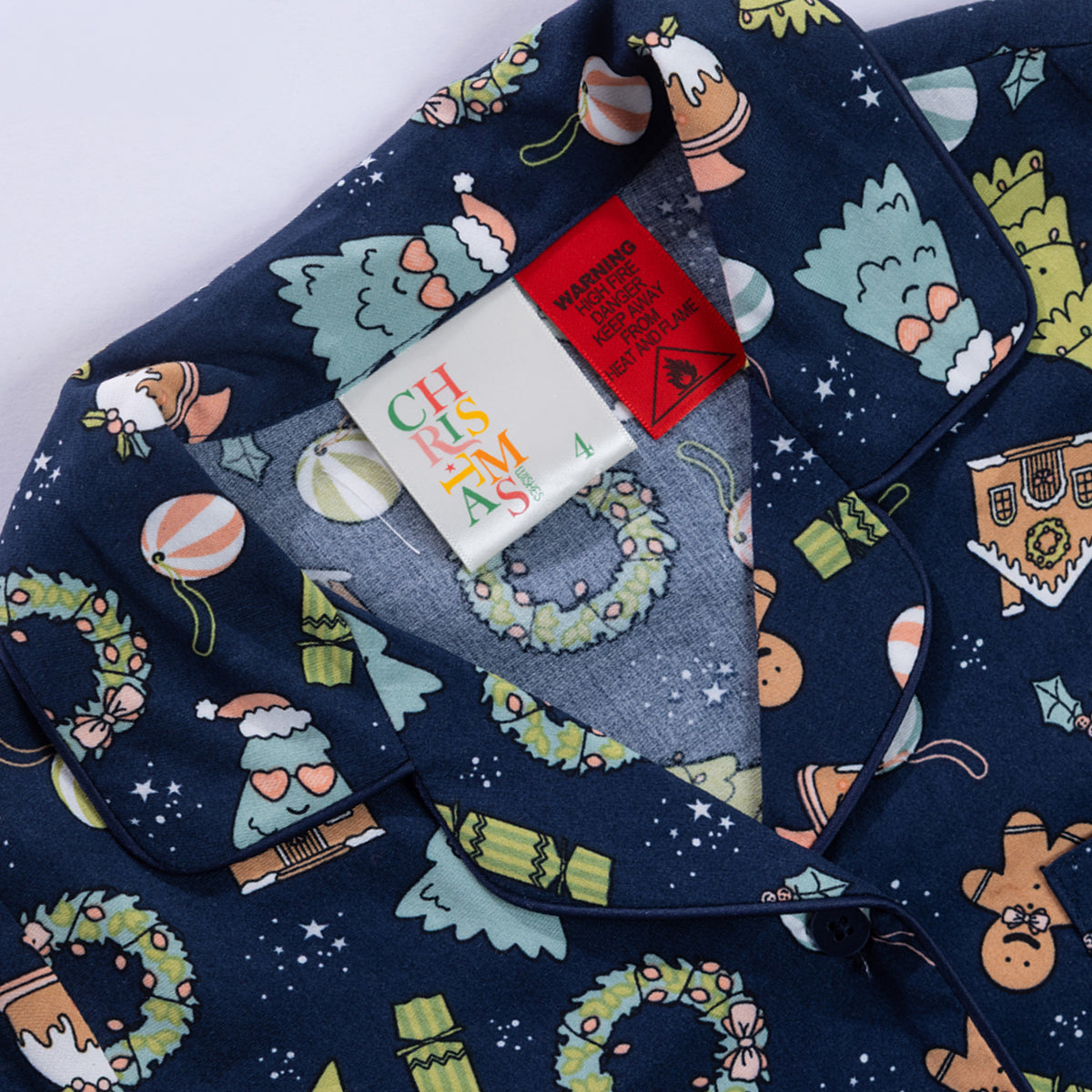 Close-up of the Christmas Wishes Wreath Kids PJ Set collar, festive print, size label and safety warning tag.
