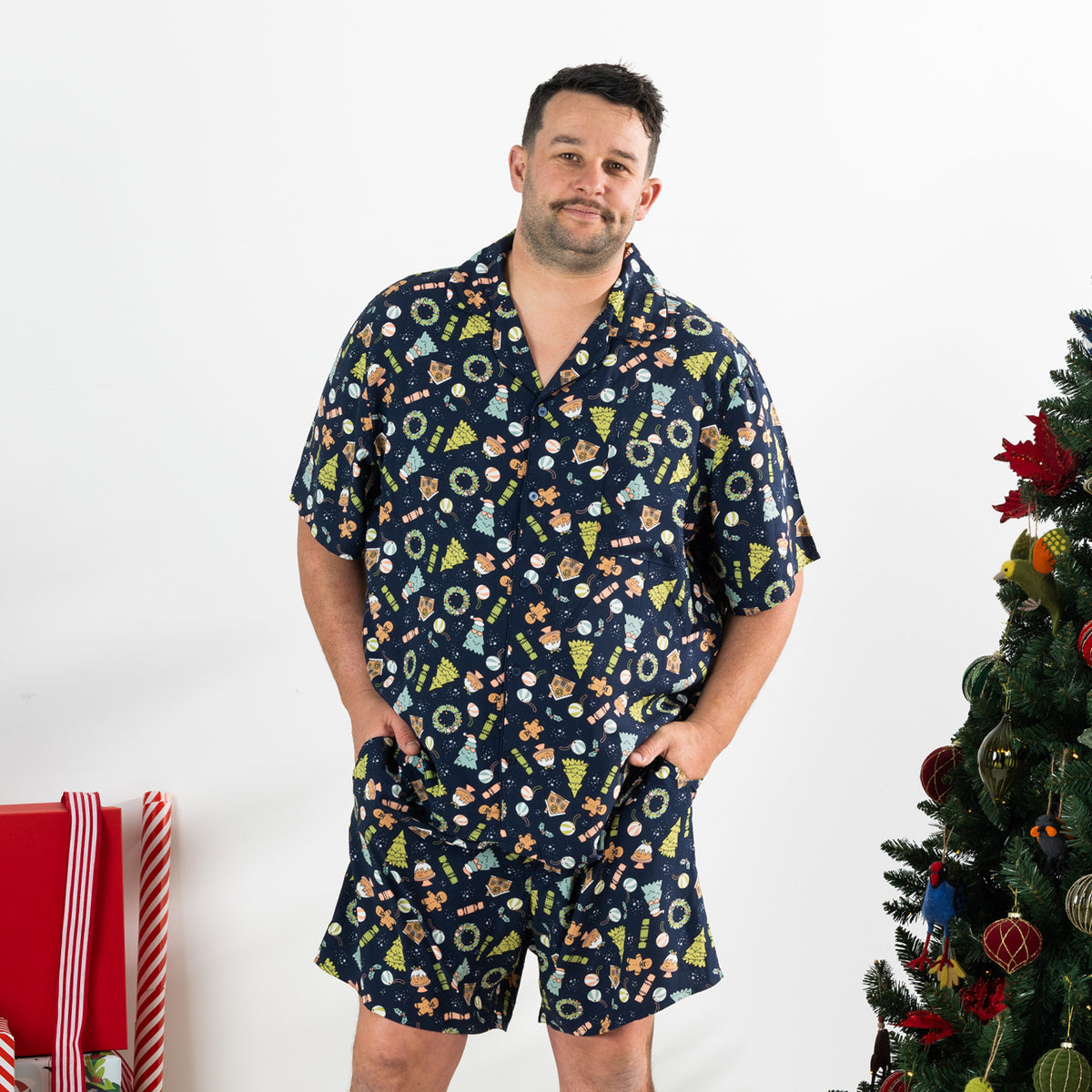 Man wearing the Christmas Wishes Wreath Men’s PJ Set in navy with a button-up short sleeve top and matching shorts.