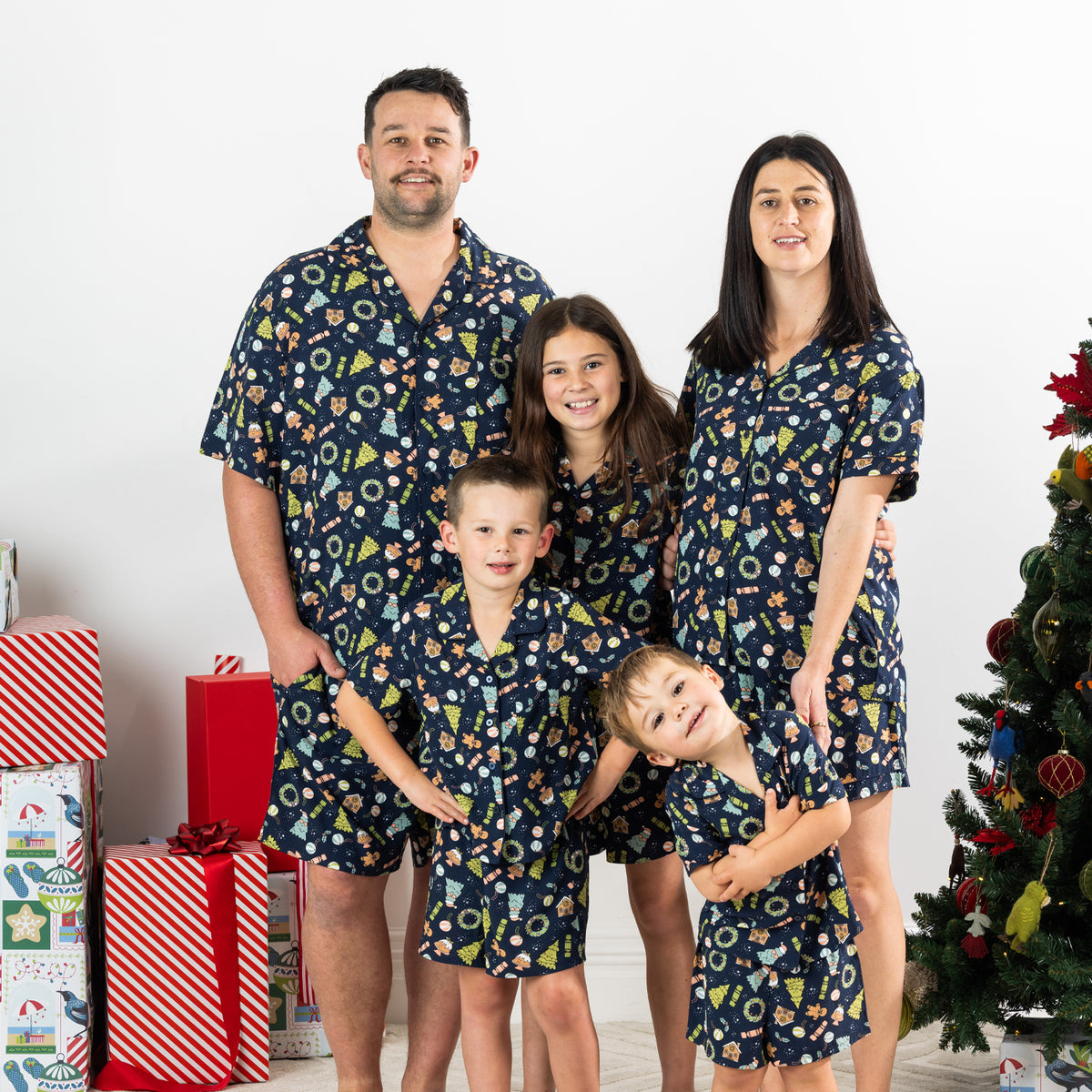 Family wearing matching Christmas Wishes Wreath PJ Sets in navy in a festive Christmas setting.
