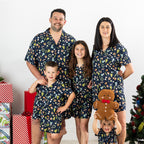 Family wearing matching Christmas Wishes Wreath PJ Sets in navy beside a decorated Christmas tree.