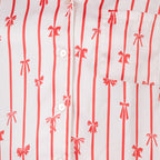 Close-up of the pink satin bow pyjama fabric featuring red vertical stripes, bow motifs, buttons and chest pocket.