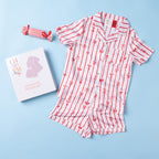 Christmas Wishes Kids’ Satin Bow PJ Set displayed with matching gift box and striped cracker-style accessory on a light blue background.