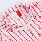 Close-up of the Christmas Wishes Kids’ Satin Bow PJ Set showing the red striped bow print, piped collar, button front and warning label.