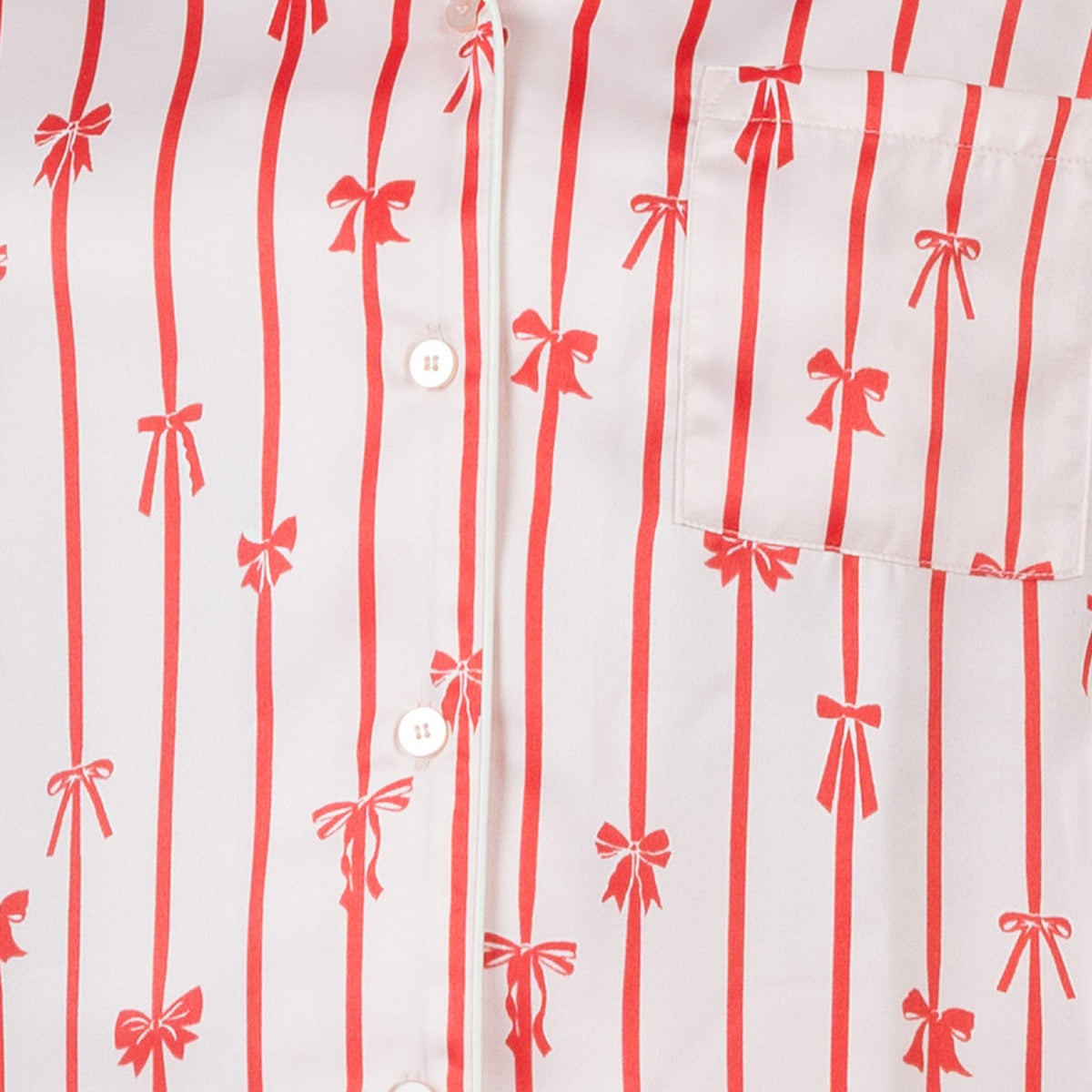 Close-up of the pink satin pyjama fabric showing red striped bow print, button front and chest pocket.