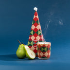 A festive Candied Pear candle with bold geometric Christmas packaging, styled alongside fresh pears against a rich blue backdrop.