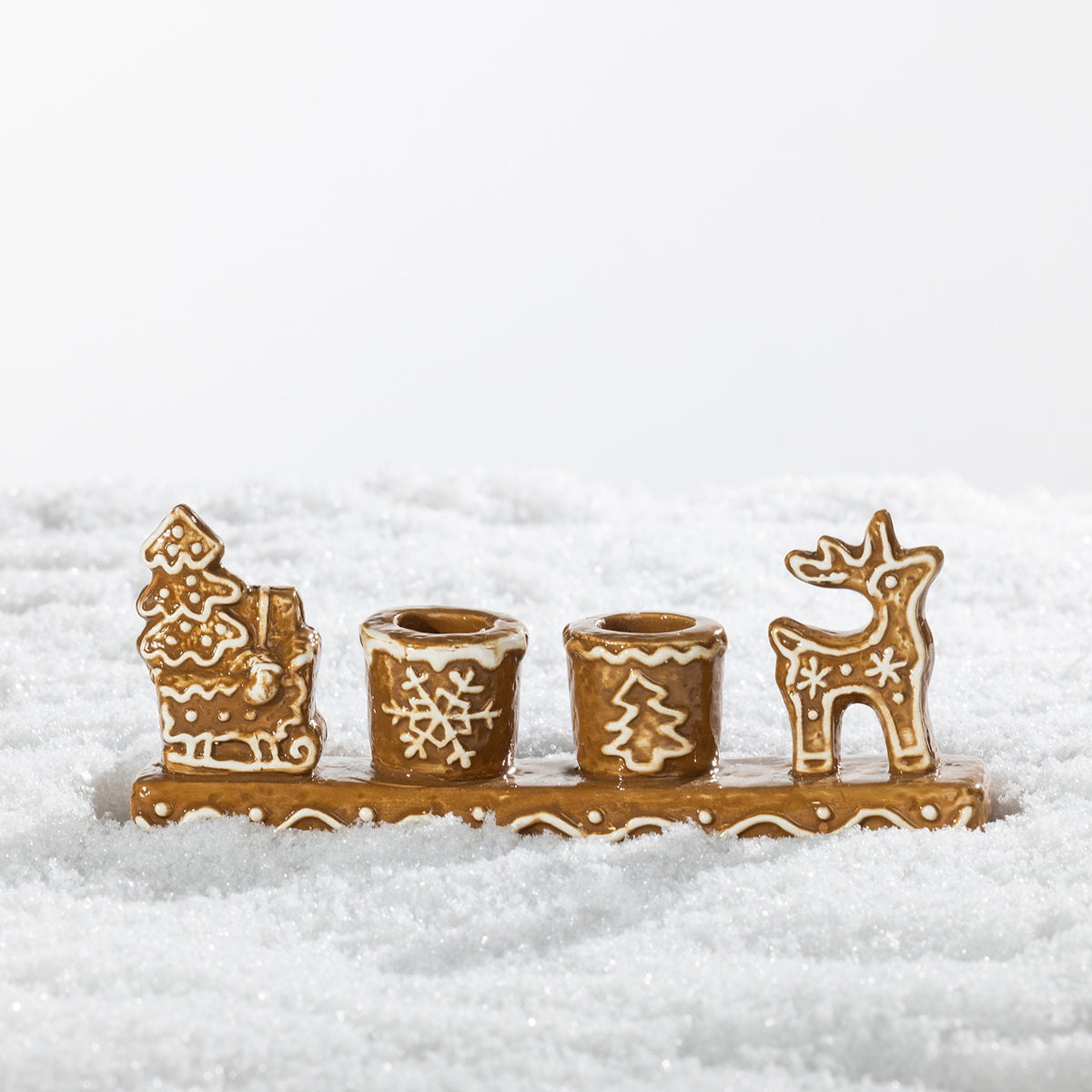 Gingerbread-style ceramic two-candle holder featuring a festive sleigh, snowflake, Christmas tree and reindeer design with white icing-inspired detailing.