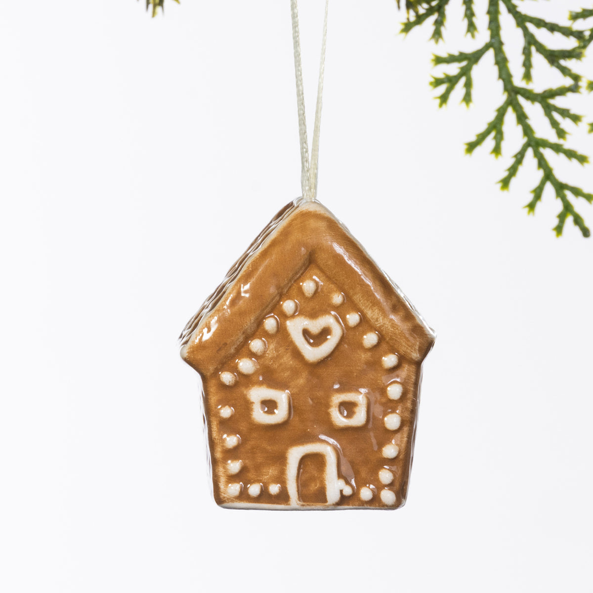 Gingerbread-style ceramic house hanging decoration with white heart and dot detailing, displayed hanging from a Christmas tree branch.