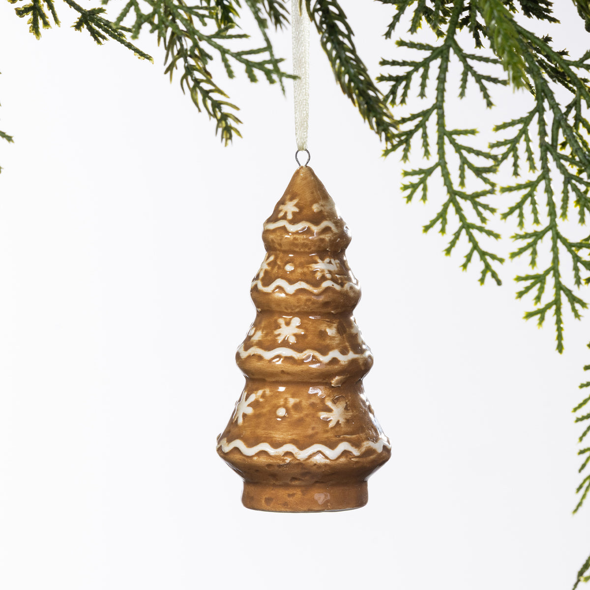 Gingerbread-style ceramic Christmas tree hanging decoration with white snowflake and zigzag detailing, displayed hanging from a Christmas tree branch.