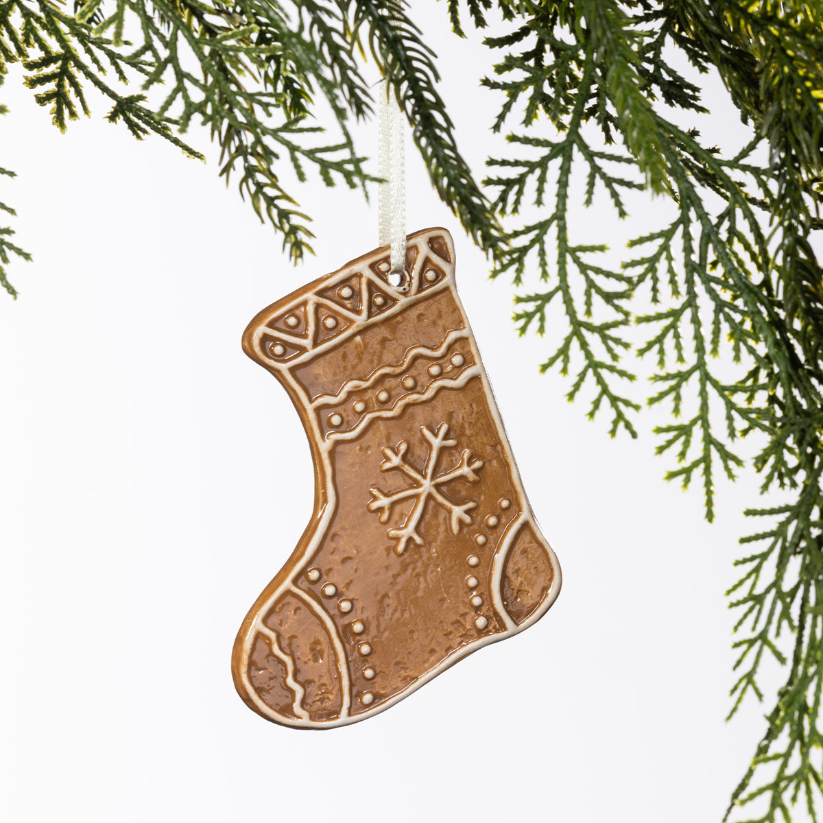 Gingerbread-style ceramic Christmas stocking hanging decoration with white snowflake and icing-inspired detailing, suspended from a cream ribbon.