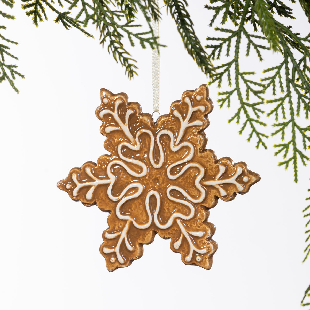 Gingerbread-style ceramic snowflake hanging decoration with intricate white icing-inspired detailing, suspended from a cream ribbon.