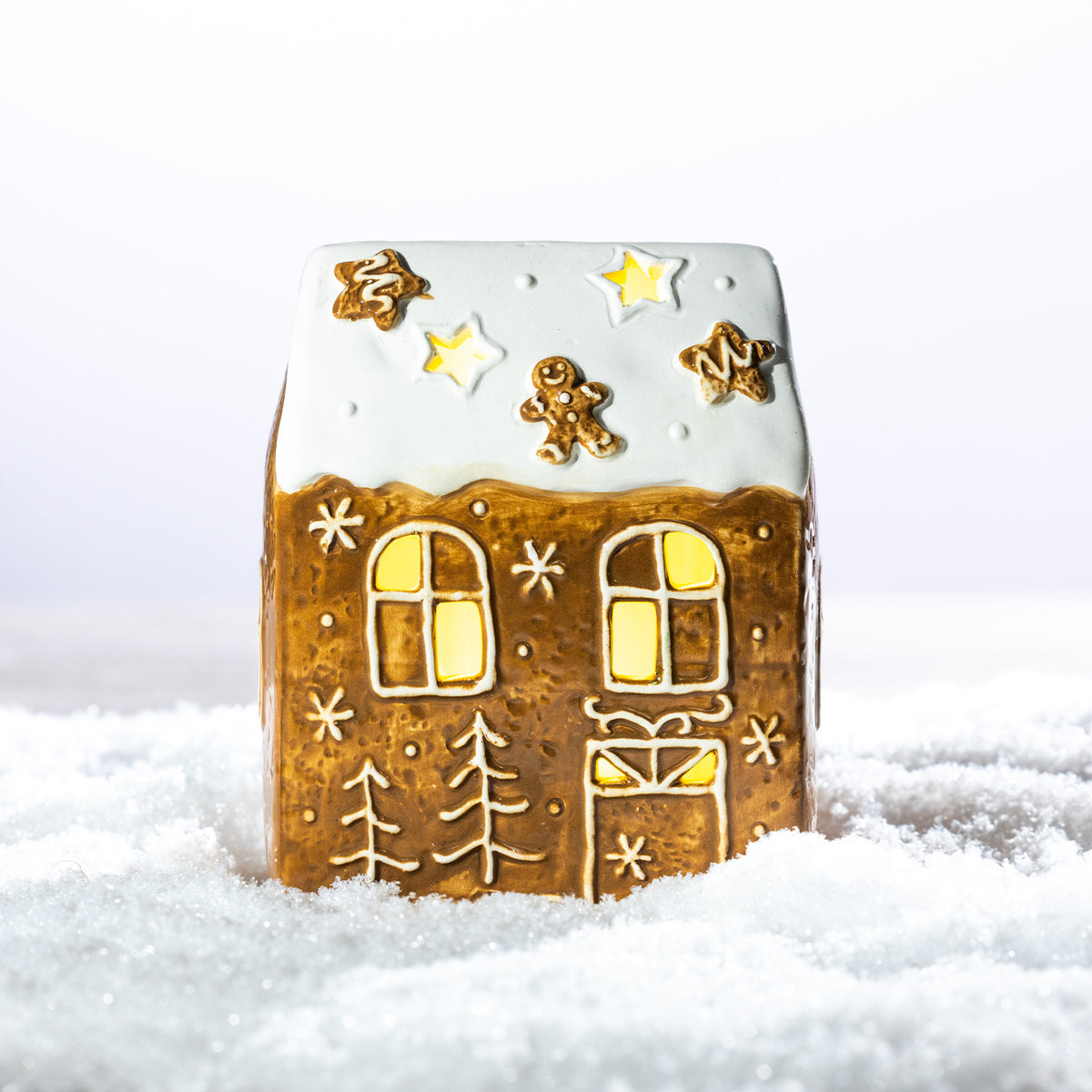 Gingerbread-style ceramic LED house displayed with coordinating gingerbread Christmas decorations in a snowy festive setting.