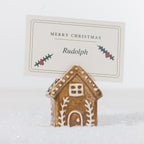 Gingerbread-style ceramic house name card holder with white icing details, holding a personalised Merry Christmas place card in a snowy setting.