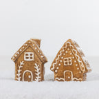 Two gingerbread-style ceramic house name card holders with white icing details displayed together in a snowy setting.