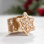 Gingerbread-style ceramic snowflake napkin ring displayed with a softly blurred festive background.