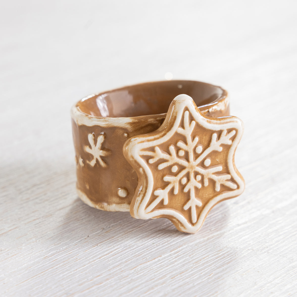 Close-up of a gingerbread-style ceramic snowflake napkin ring with white icing details.