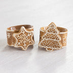Gingerbread-style ceramic napkin rings featuring snowflake and Christmas tree designs displayed together.