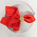 Gingerbread-style ceramic snowflake napkin ring holding a bright red napkin on a white plate.