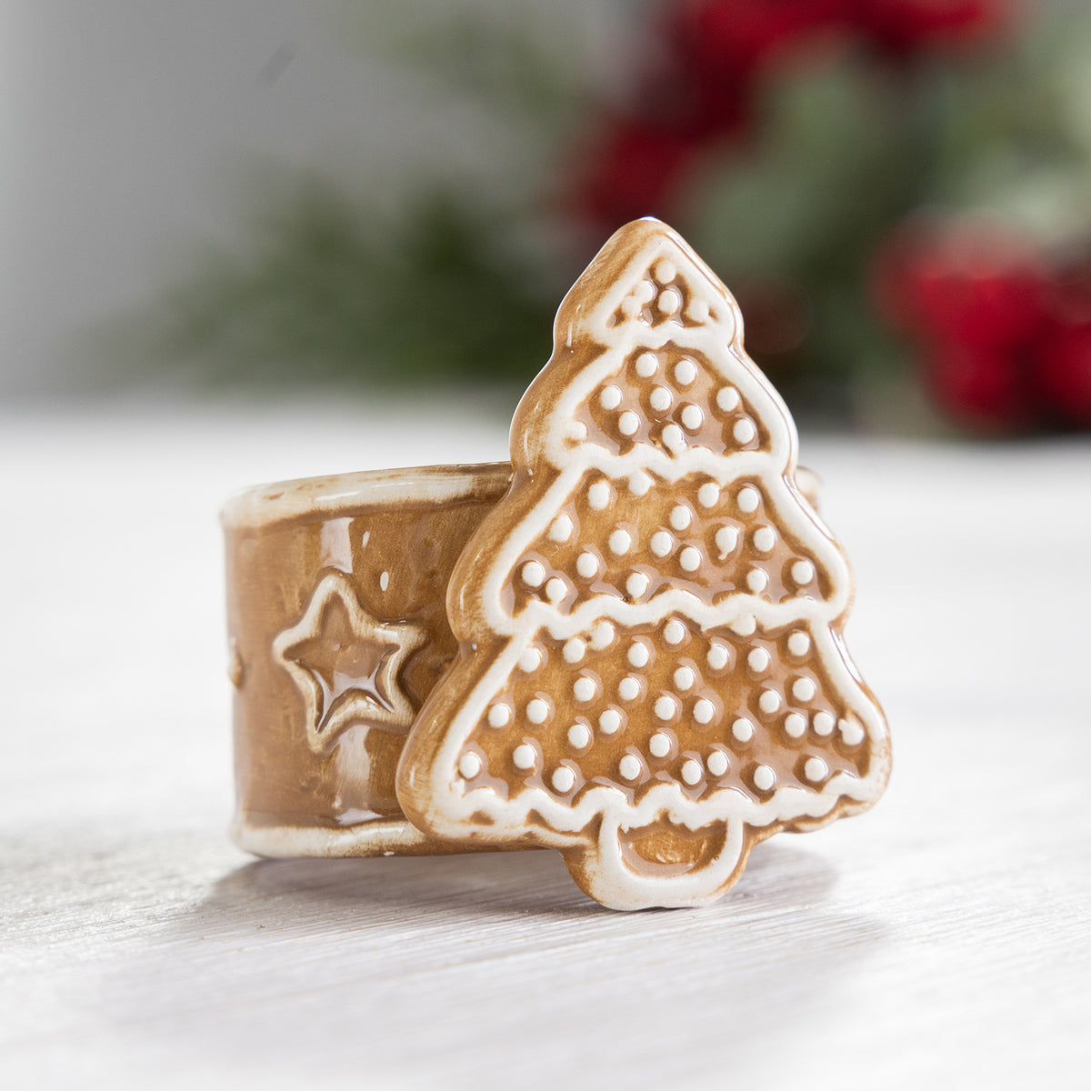 Gingerbread-style ceramic Christmas tree napkin ring displayed with a softly blurred festive background.