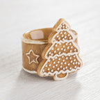 Gingerbread-style ceramic Christmas tree napkin ring with white icing details on a light timber surface.
