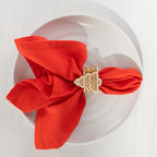 Gingerbread-style ceramic Christmas tree napkin ring holding a bright red napkin on a white plate.