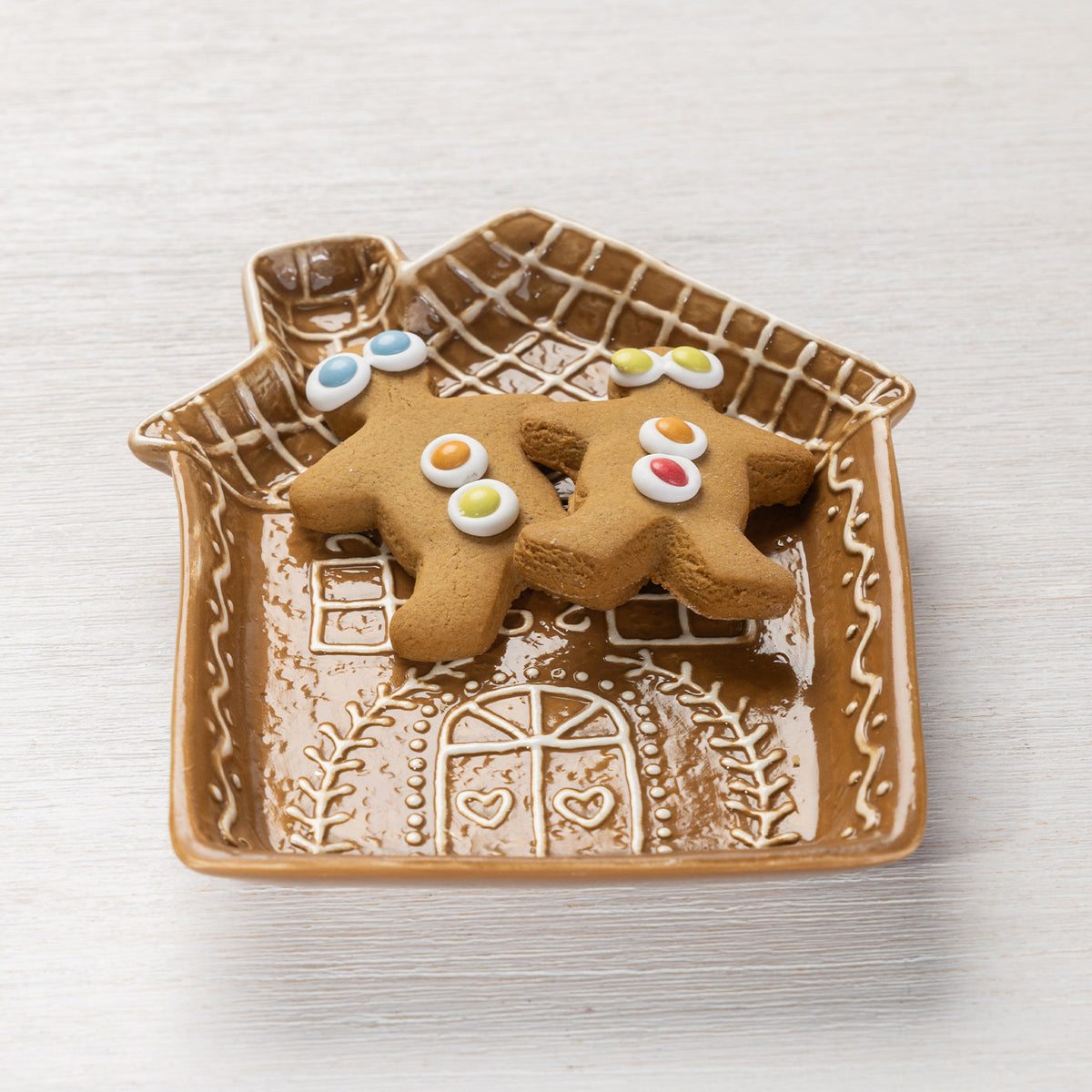Gingerbread house-shaped ceramic trinket plate filled with two decorated gingerbread biscuits.
