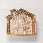 Angled view of a gingerbread house-shaped ceramic trinket plate with raised roof, window and door details.