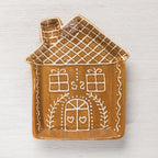 Gingerbread house-shaped ceramic trinket plate with white icing-style details on a light timber surface.