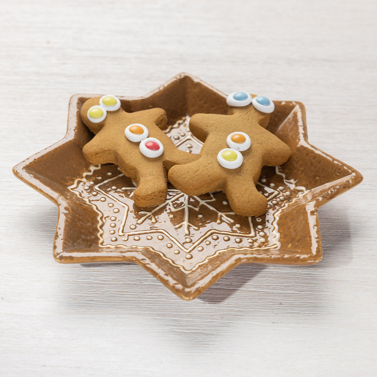 Star-shaped gingerbread-style ceramic trinket plate holding two decorated gingerbread biscuits.