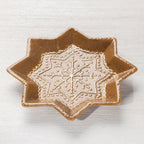 Angled view of the gingerbread-style star-shaped ceramic trinket plate with white snowflake detailing.