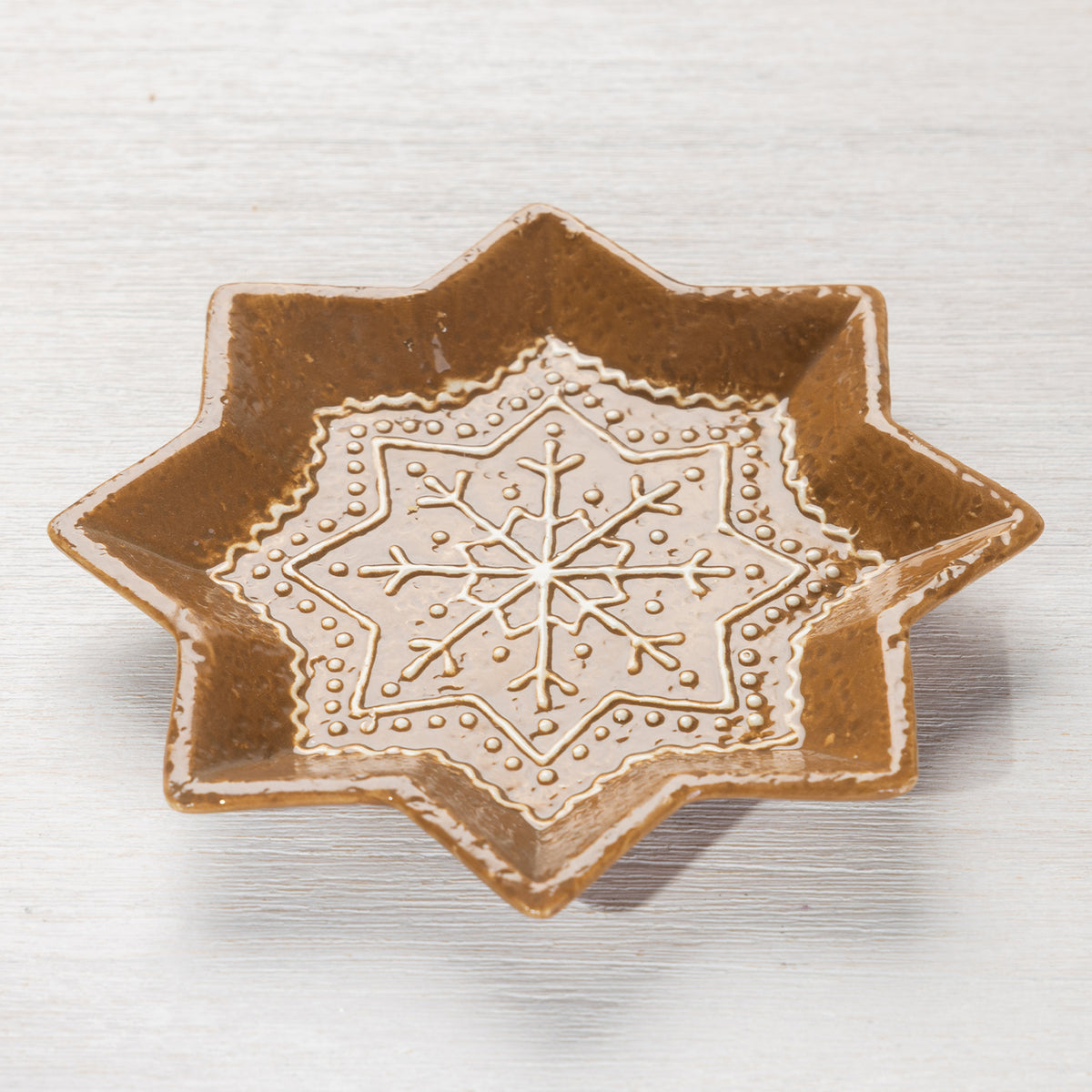 Angled view of the gingerbread-style star-shaped ceramic trinket plate with white snowflake detailing.