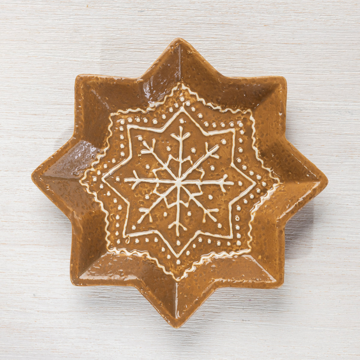 Top view of a star-shaped ceramic trinket plate with a detailed white snowflake design.