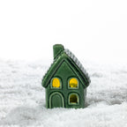 Small green ceramic house LED decoration glowing warmly in a snowy festive setting.