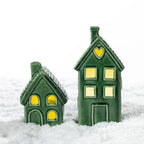 Small and tall green ceramic house LED decorations glowing together in a snowy festive setting.