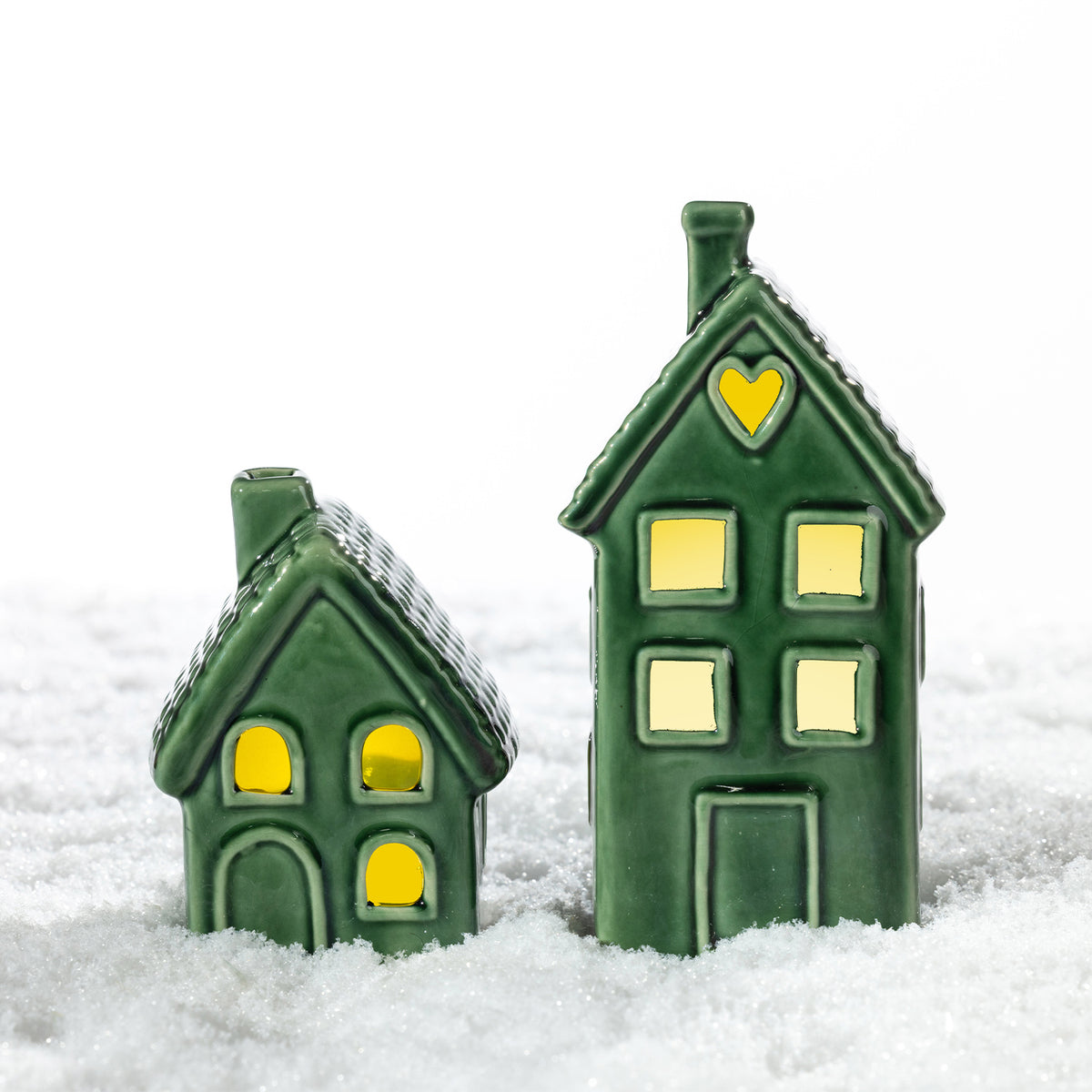 Small and tall green ceramic house LED decorations glowing together in a snowy festive setting.