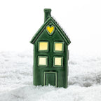 Tall green ceramic house LED decoration with glowing windows and a heart-shaped cut-out, displayed in a snowy festive setting.