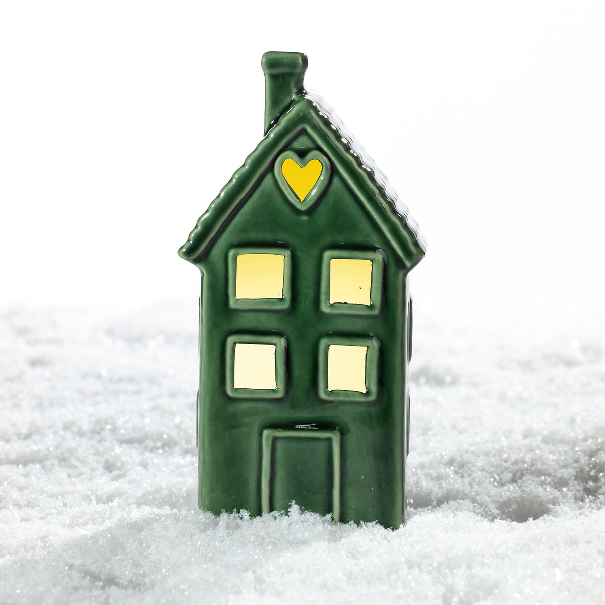 Tall green ceramic house LED decoration with glowing windows and a heart-shaped cut-out, displayed in a snowy festive setting.