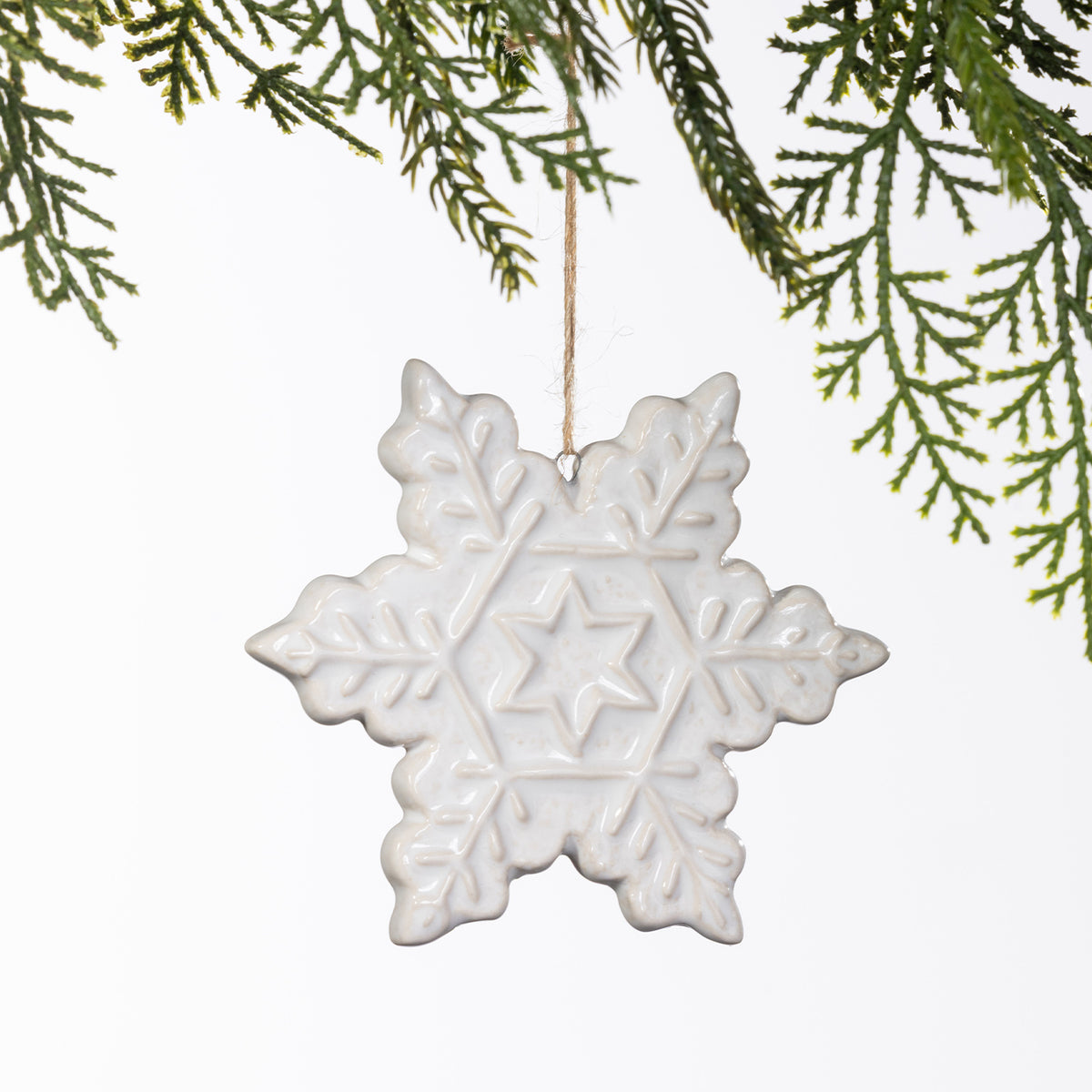 White ceramic snowflake hanging decoration with embossed snowflake detailing, suspended from a natural twine loop.