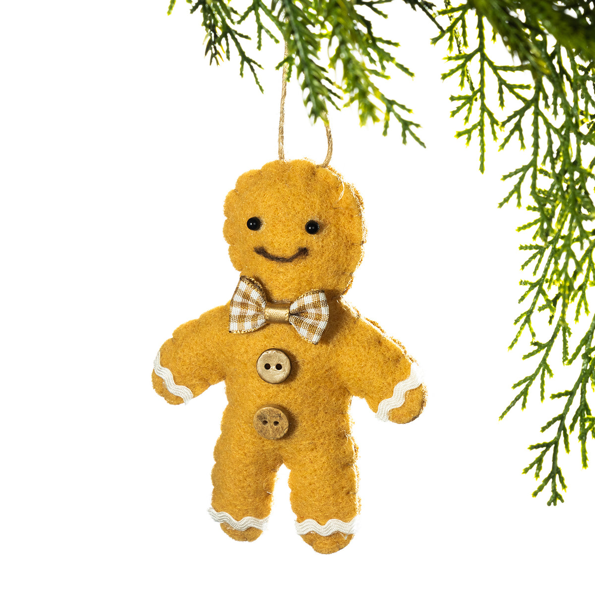 A gingerbread man felt Christmas ornament hanging from a green pine branch against a white background.