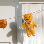 A felt gingerbread man ornament hanging from a string, with a matching felt ornament partially visible on the left, set against a white paneled background.