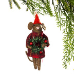 A plush Christmas mouse ornament wearing a red hat and red dress, holding a green wreath with red ornaments, hanging against a white background with pine branches framing the top and right side.