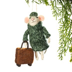 A felted wool Christmas ornament shaped like a mouse wearing a green knit sweater and hat, holding a brown suitcase, hanging against a white background with green pine branches at the top right.