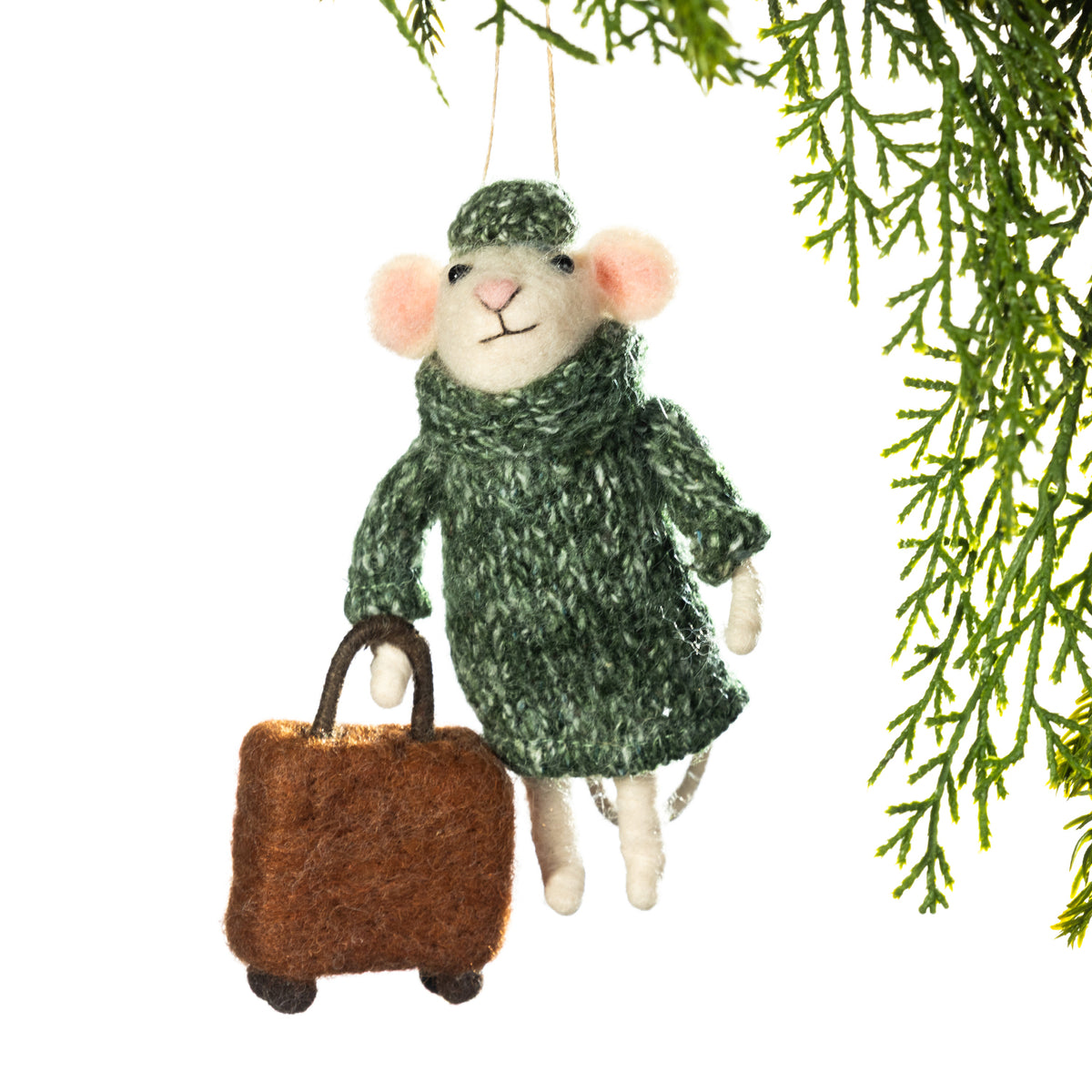 A felted wool Christmas ornament shaped like a mouse wearing a green knit sweater and hat, holding a brown suitcase, hanging against a white background with green pine branches at the top right.